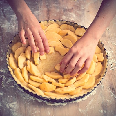 Young girl's hands arranging apples on apple pie